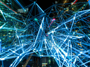 A complex network of interconnected neon blue lines and nodes, creating a futuristic web over a blurred background of lighted skyscrapers