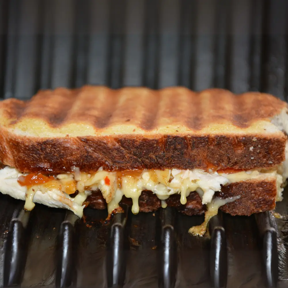 A cheese toastie on a grill rack with cheese oozing out