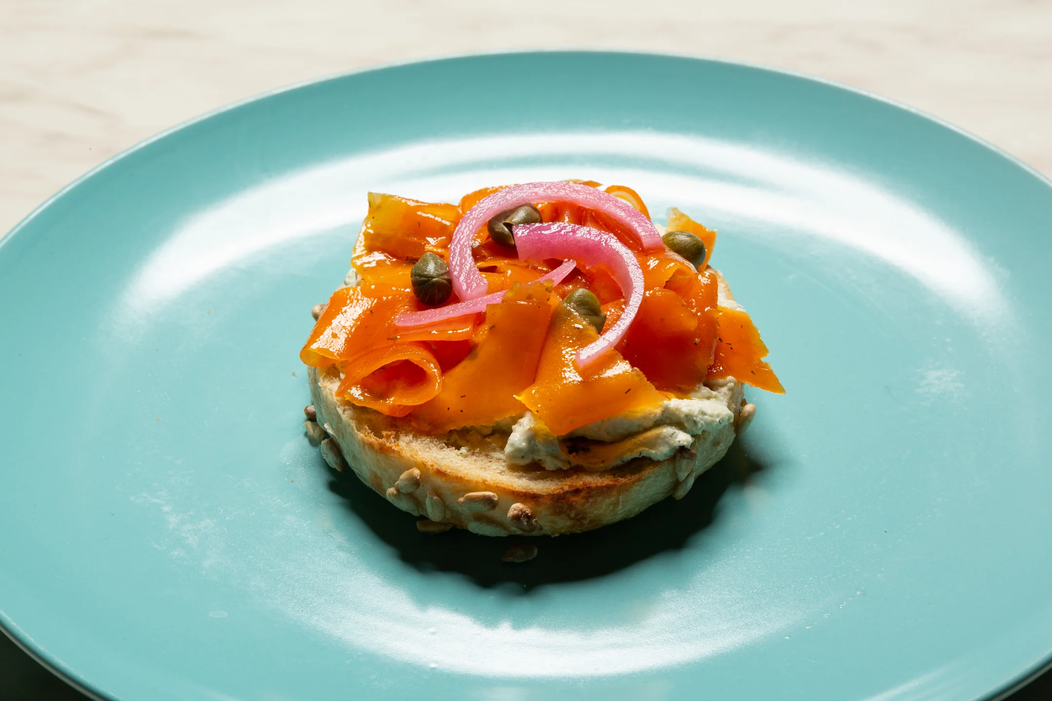 A bagel with carrot lox, sitting on a blue plate