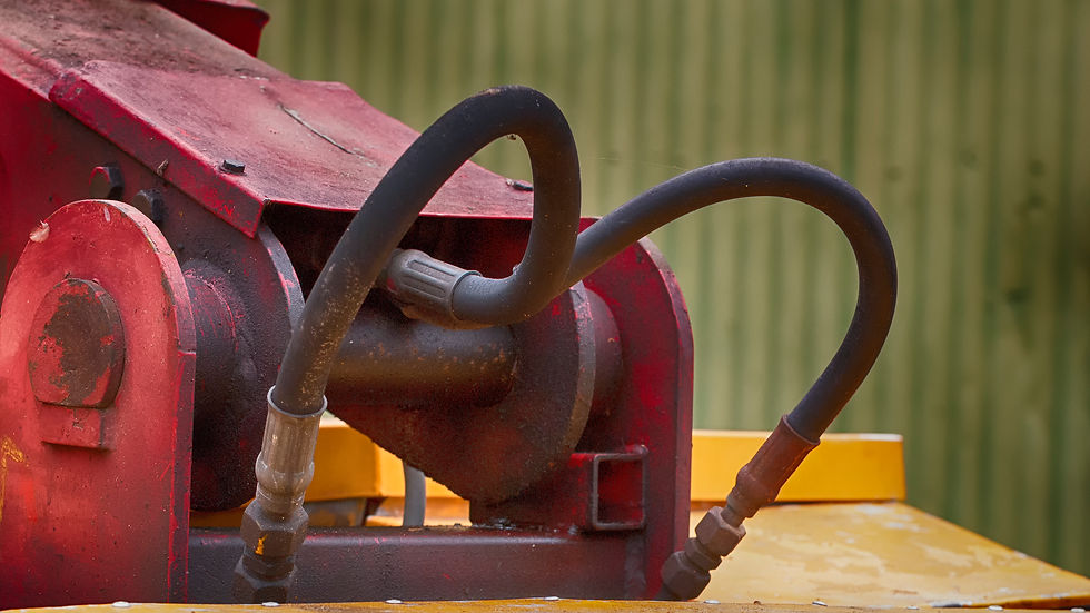 Red hydraulic machinery with black hoses on a yellow base. The background is a green corrugated surface, conveying an industrial setting.