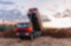 A red dump truck unloading soil on construction site