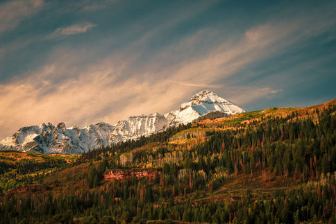 Golden autumn aspen trees with snow-capped Colorado mountains under a dramatic sky