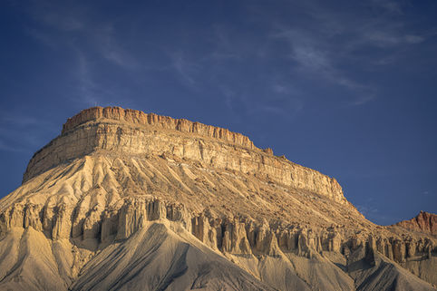Mount Garfield in the Book Cliffs of Colorado capturing golden sunset light on layered sandstone formations against deep blue sky.