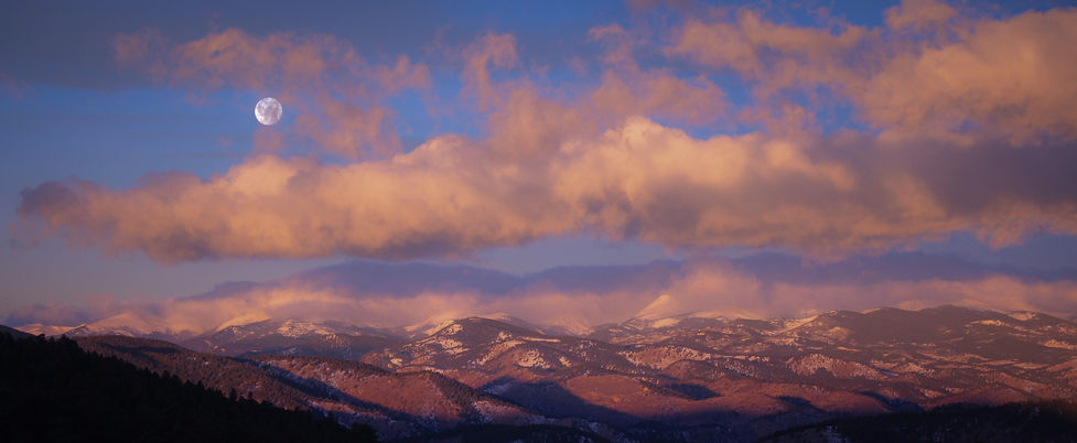 Full moon setting over snow-capped Rocky Mountains at dusk with pink-tinged clouds and purple-blue twilight sky - perfect for Colorado wilderness photography, mountain landscape inspiration, and Rocky Mountain National Park scenic vistas.