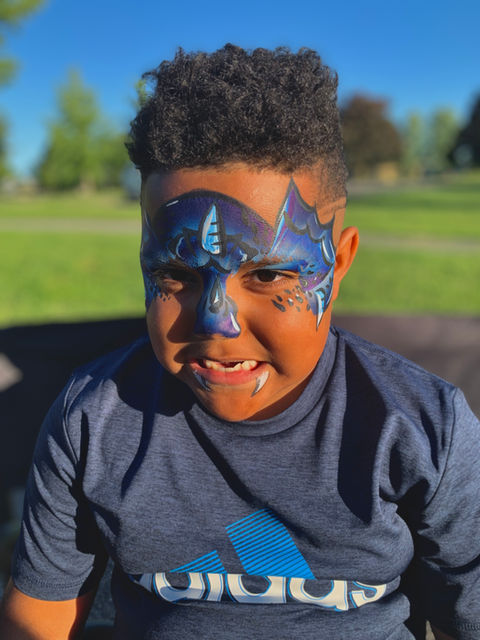 A child showcasing their vibrant dragon face paint with a fierce dragon snarl. The blue and teal colors radiate joy and cheerfulness. Experience the magic of our talented artists' colorful creations and book with GoFacepaint today! We service Durham Ontario, London Ontario, and Montreal Quebec.