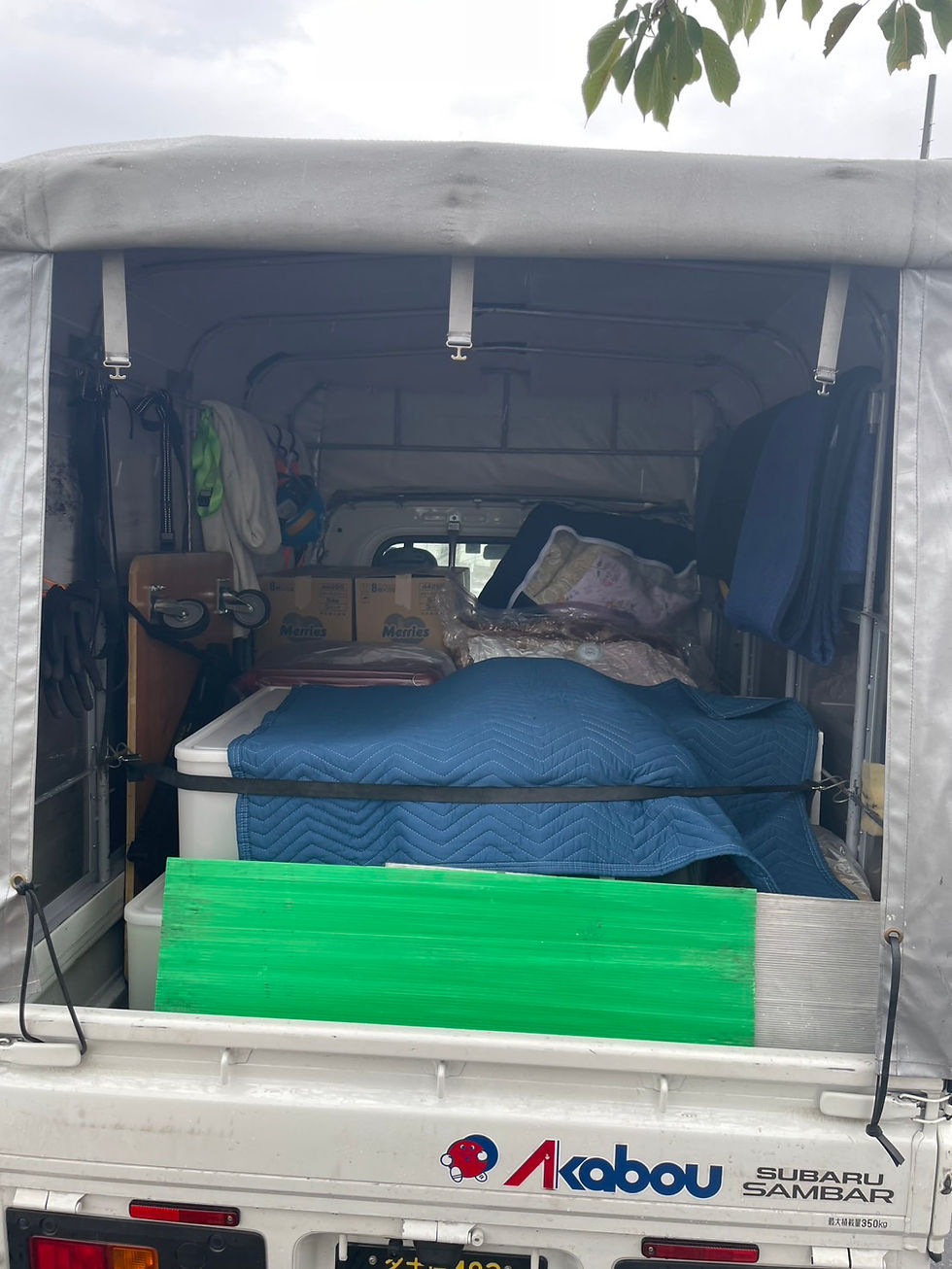 雨の日の引っ越しで、赤帽の幌付き軽トラックの荷台に段ボールや衣装ケースを積み、青い毛布とベルトで荷物を保護・固定している様子。