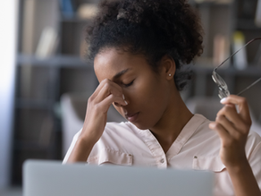 exhausted woman in front of a laptop holding her head in one hand and glasses in the other