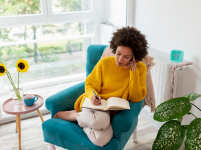 woman wearing a yellow sweater sitting on a turqouise chair writing in a book