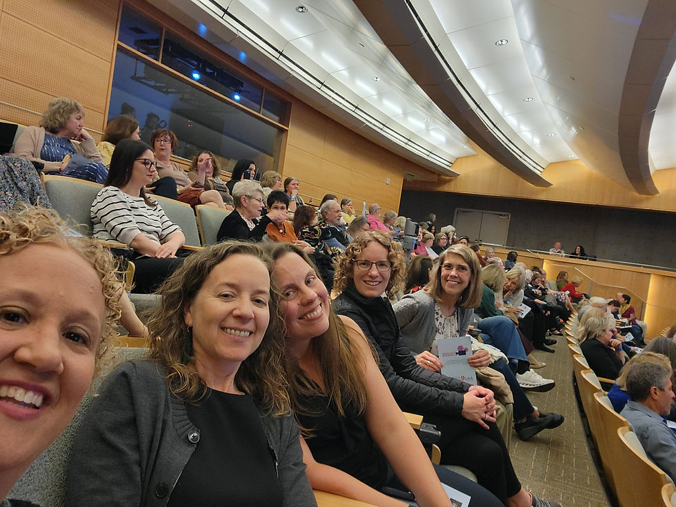 5 smiling women, posed together, in an auditorium with a crowd in the background