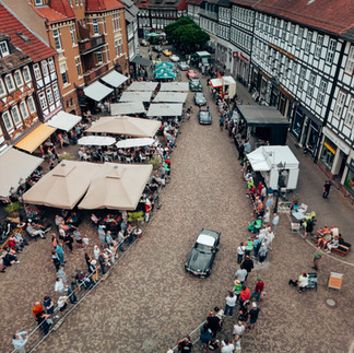 Luftaufnahme eines Altstadt-Marktplatzes mit Fachwerkhäusern, Marktständen und einer Oldtimer-Parade.