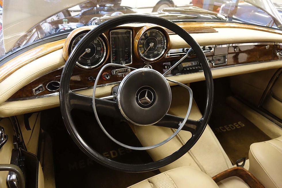 Innenraum eines klassischen Mercedes-Benz mit cremefarbenen Ledersitzen, Holzarmaturenbrett und großem Lenkrad mit Mercedes-Stern.