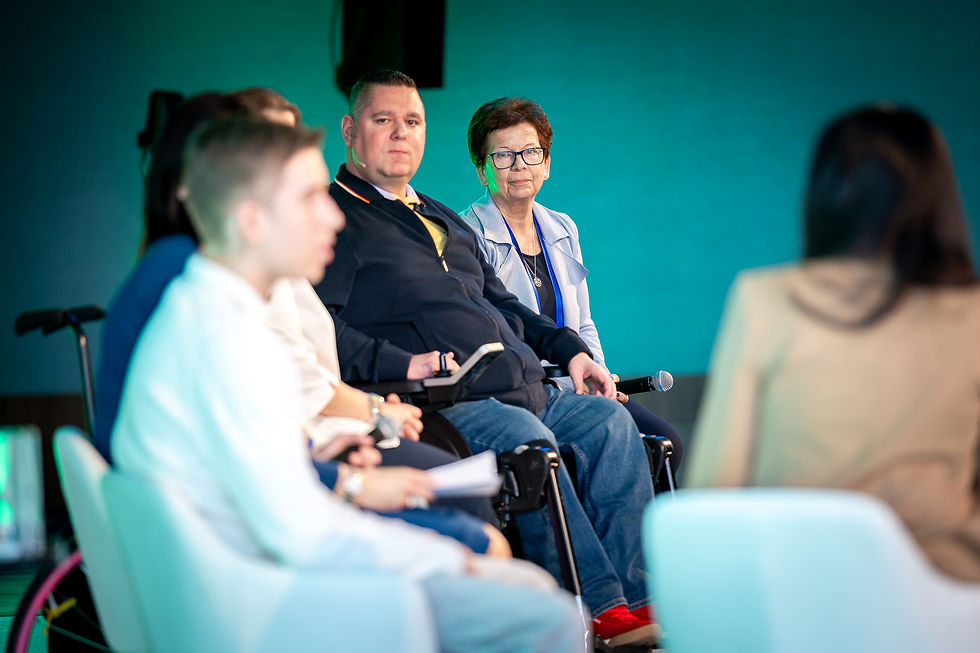 Panel discussion with seated man and woman holding microphones, surrounded by blurred audience in a teal-lit room.