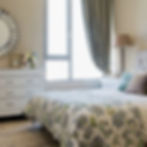 Side view of a cozy bed with a botanical bedcover and styled which chest of drawers.