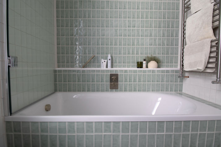 Bath with mint wall tiles, inward-folding glass screen and heated towel rail, Surrey family bathroom