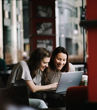 Duas mulheres sorridentes sentadas em frente a um computador num ambiente de trabalho minimalista.