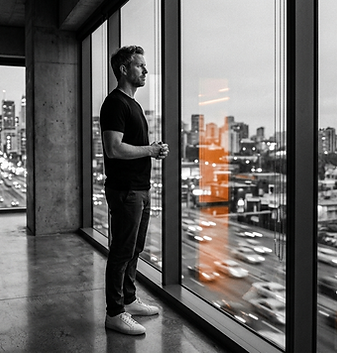 Homem refletindo em pé um frente a uma grande janela de um edifício empresarial como se estivesse pensando no futuro
