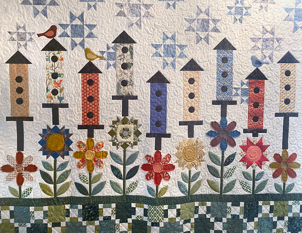 Thumbnail: Alternate view of Morningside, a scrappy birdhouse quilt pattern, features brightly colored bird houses above applique flower