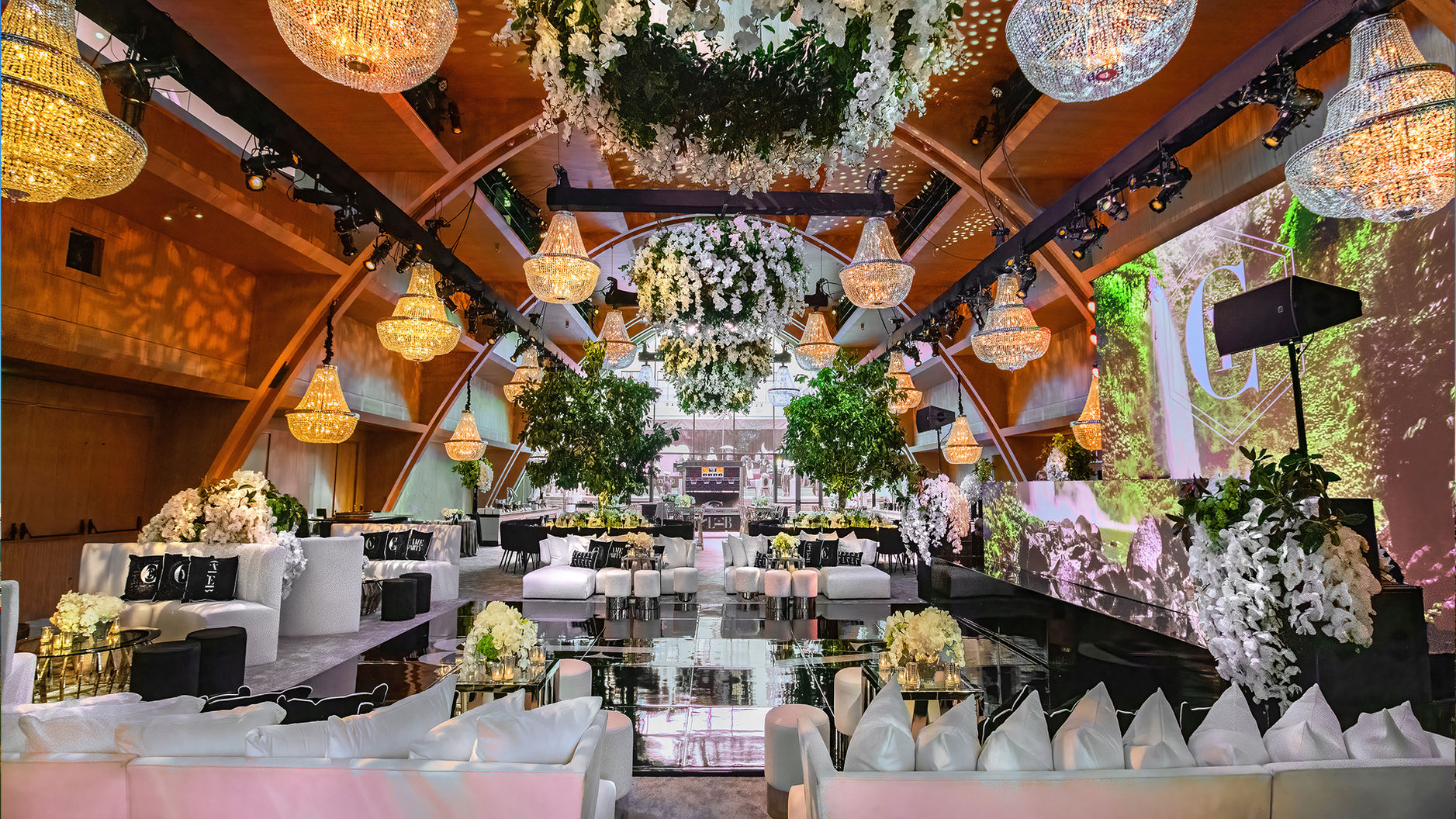 An interior view of the Audrey Irmas Pavilion at the Wilshire Boulevard Temple. The room is set up for a reception, with chandeliers and flowers hung throughout.