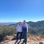 Happy couple smiling together at Juniper Flats overlook with dramatic mountain views and clear blue sky behind them.