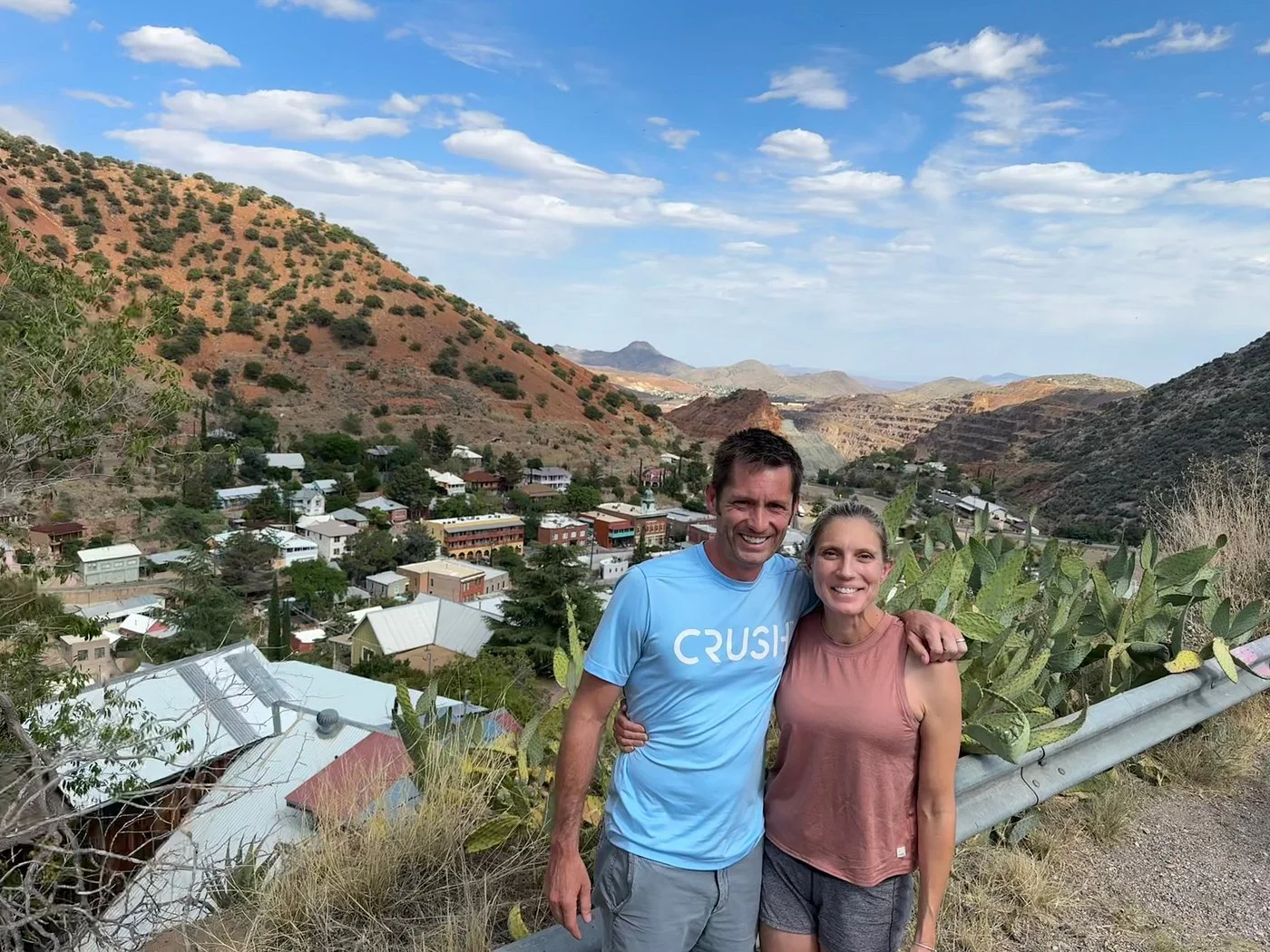 Smiling couple posing together at high road overlook with panoramic view of Bisbee town and mountains.