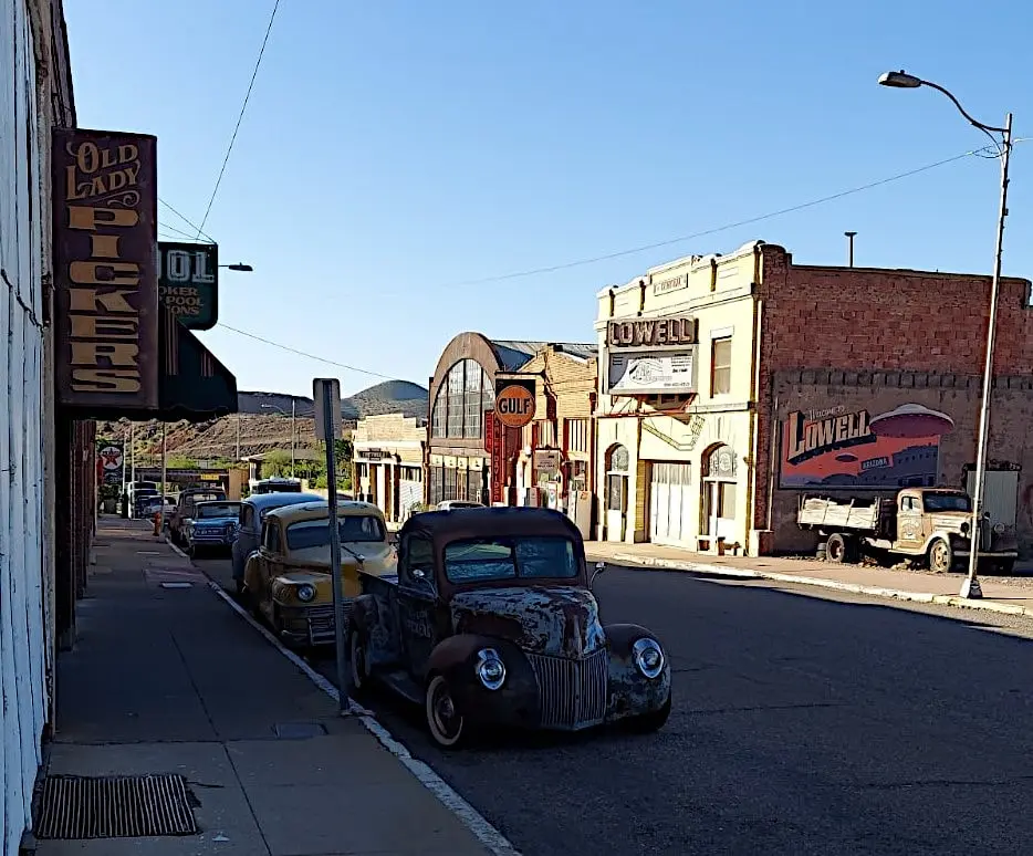 Classic trucks and cars parked in the shade along the street with vintage storefronts.
