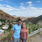 A happy couple poses on a hillside overlooking the historic buildings, streets, and desert mountains of Old Bisbee, Arizona during an outdoor adventure tour.