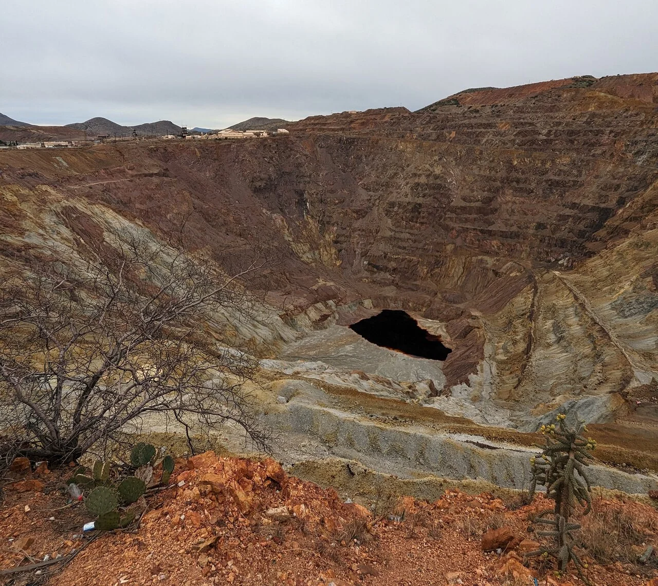 Open mine pit with black water at the bottom and a cloudy sky.