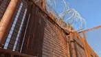 Tall metal border wall topped with coils of razor wire under clear blue sky in Naco, Arizona.