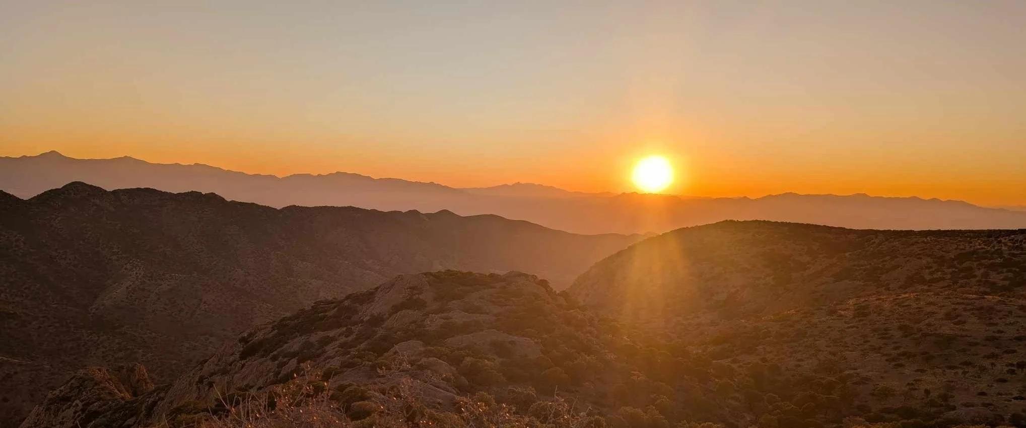 Golden sunset with bright sun on horizon casting rays over layered mountain ridges from Juniper Flats viewpoint.