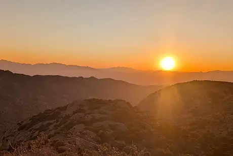 Golden sunset over layered mountain ranges from Juniper Flats in Bisbee Arizona with the bright sun on the horizon and rocky foreground.