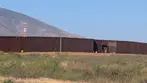 Long brown border wall stretching across desert landscape with mountains in background near Naco.