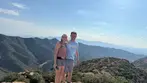 Smiling couple standing on a rocky mountain overlook with panoramic desert valley views during a Big Jeep Tours adventure.