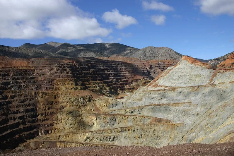 Vast terraced Lavender Pit mine with colorful layered rock walls under bright blue sky with scattered clouds.