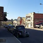 Vintage classic cars parked along Erie Street in Lowell Bisbee with historic brick buildings and clear blue sky.
