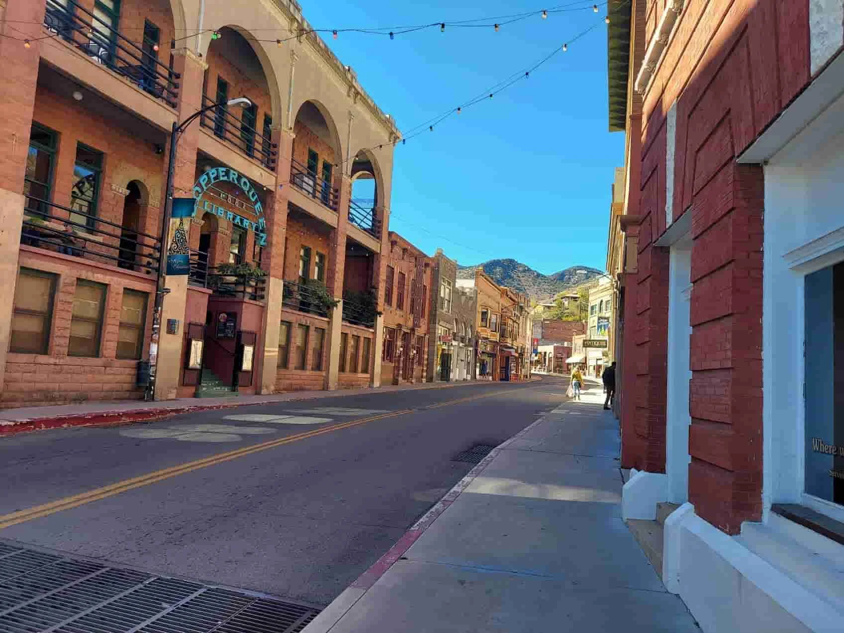 Sunny Main Street in Bisbee lined with historic brick buildings and Copper Queen Library sign under clear blue sky.