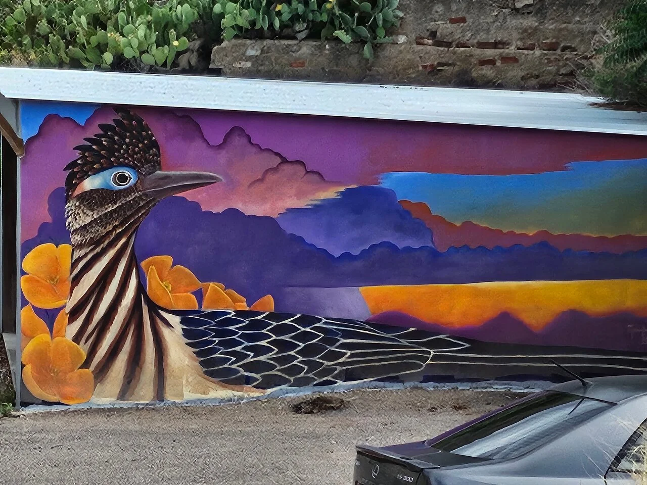 Colorful roadrunner mural with purple sunset sky and orange poppies painted on wall in Bisbee.