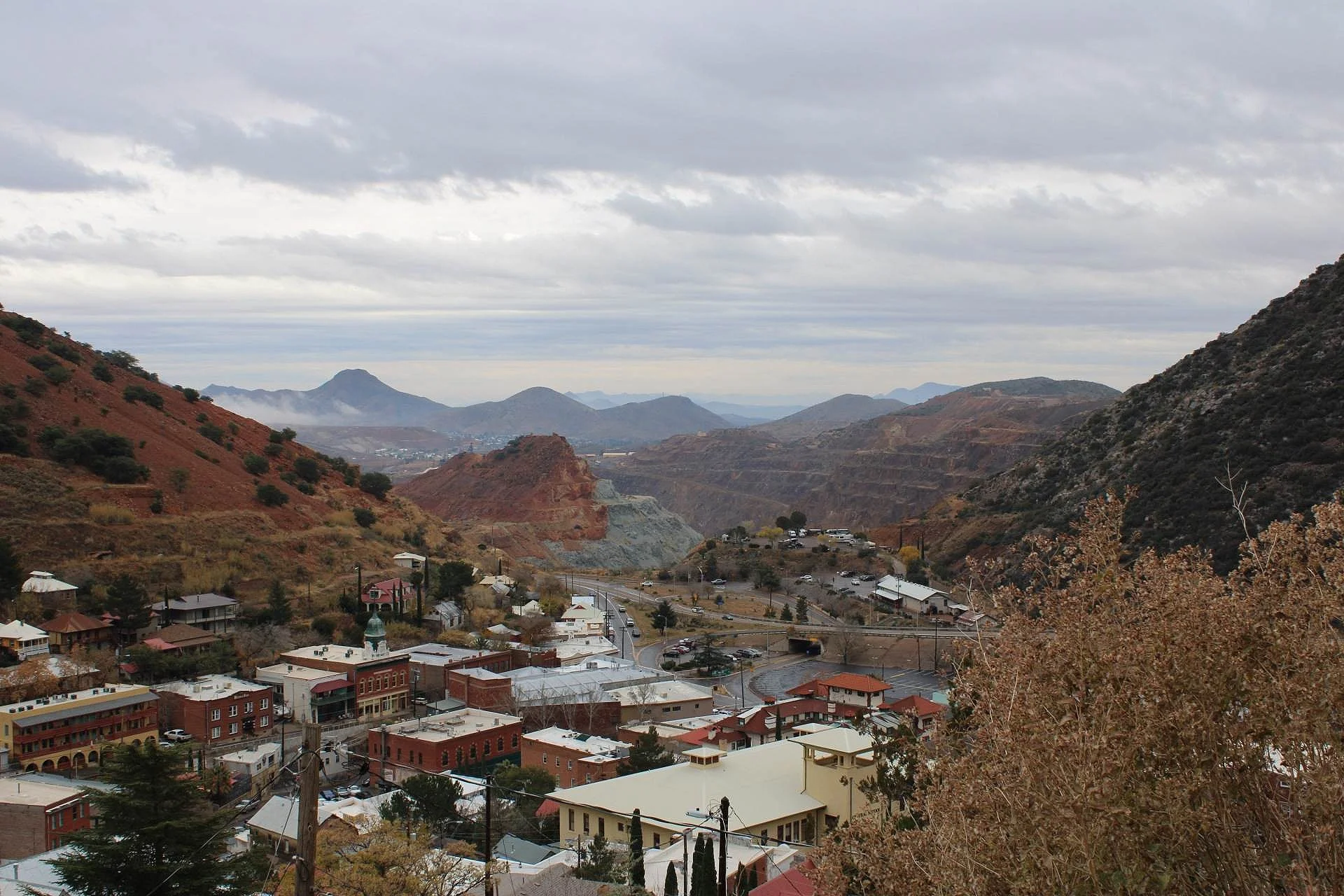 Panoramic mining valley overlook of Bisbee town nestled in colorful hills and mountains under partly cloudy sky.
