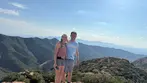 Smiling couple standing on a rocky mountain overlook with panoramic desert valley views during a Big Jeep Tours adventure.