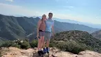 Smiling couple standing on rocky Mule Mountains summit with vast mountain panorama behind them.