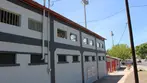 White and gray Warren Ballpark grandstand building with tall light tower under blue sky.