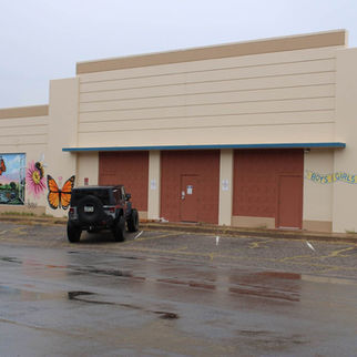 Exterior view of the Boys & Girls Club of Bisbee building on a rainy day, showcasing a colorful mural with flowers and butterflies, with a Big Jeep Tours vehicle parked outside.