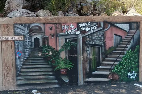 Mural of stairs and buildings with text Fly to Europe or Drive to Bisbee painted on wall.