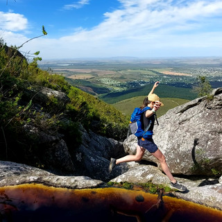 trail runner jumping across a river with a view