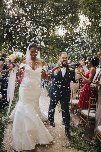 Bride and groom walking down the aisle as guests throw flower petals during an outdoor wedding ceremony at Casa dos Penedos in Sintra, Portugal.
