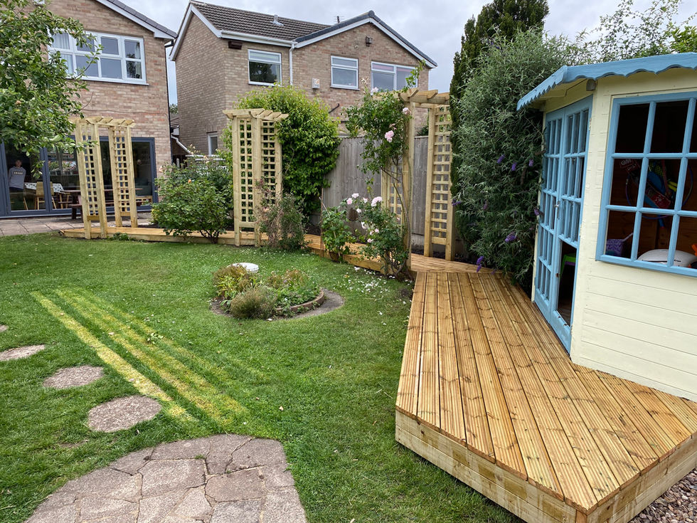 Wooden deck and garden with wooden structures; green grass and bushes.