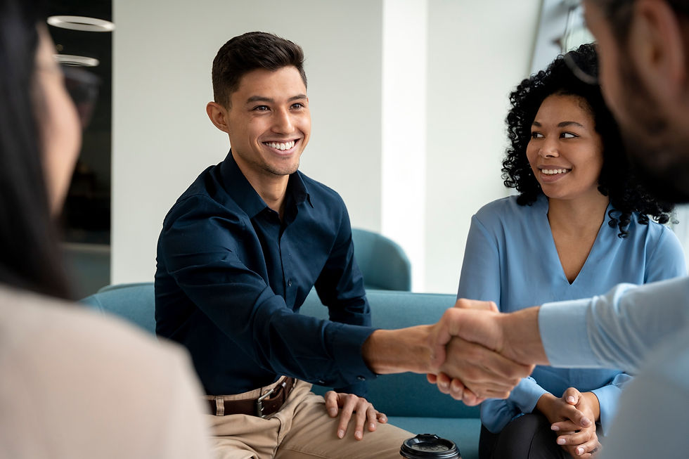 Smiling people sit on blue couches in an office. Two people shake hands, creating a friendly and professional atmosphere.