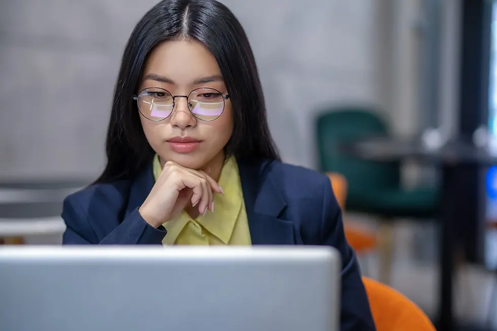 Woman with glasses works intently on a laptop in a modern cafe, Reflections visible in her lenses.
