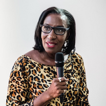 Woman with glasses and microphone, leopard print top, speaking at event