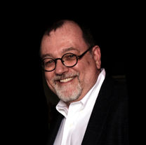 Smiling man with glasses and beard, wearing a suit jacket.
