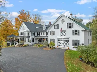 image of a black and white inn with a grey gazebo and front porch. The picture was take in Autumn and leaves are orange.